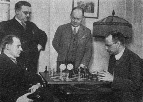 Dr. Aljechin (links) und Nimzowitsch am Schachbrett, mit Dr. Vidmar und Spielmann die zuschauen.